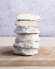 Whole and cut pieces of selles sur couffy goat's cheese stacked up on a woooden chopping board.