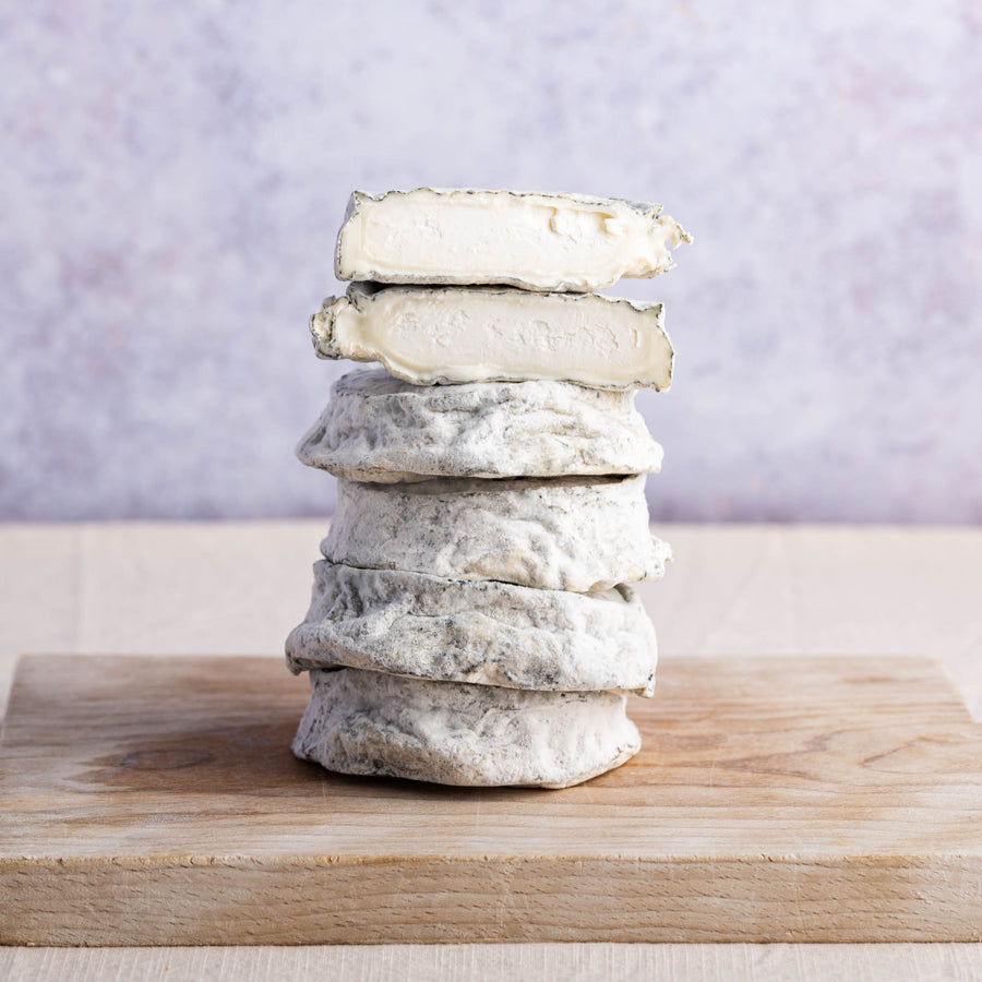 Whole and cut pieces of selles sur couffy goat's cheese stacked up on a woooden chopping board.