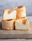 Pieces of whole and cut Langres cheese stacked up on a wooden board.