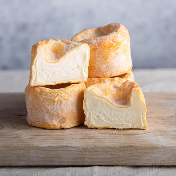 Pieces of whole and cut Langres cheese stacked up on a wooden board.