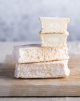 Cut and whole pieces of Lingot des Causses goat's cheese on a wooden board.