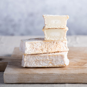 Cut and whole pieces of Lingot des Causses goat's cheese on a wooden board.