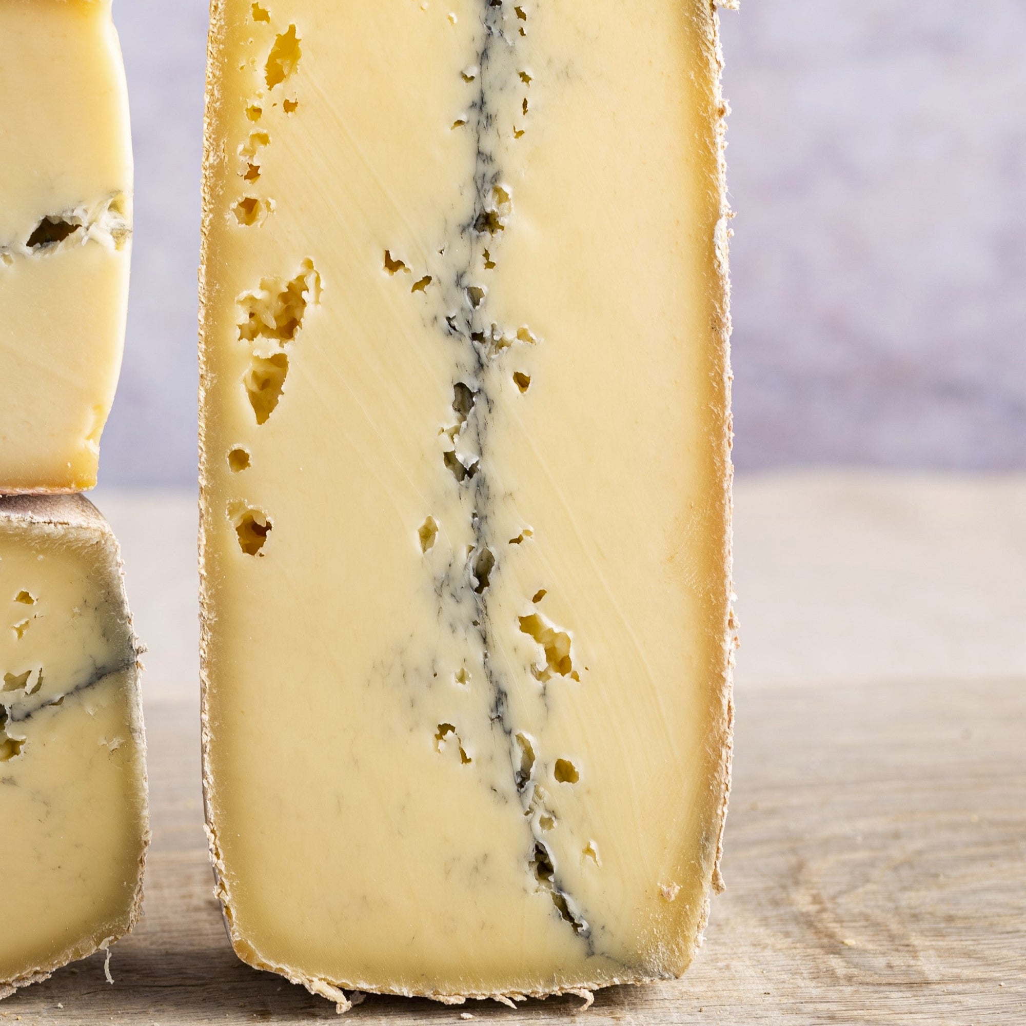 A piece of Morbier cheese, with its distinctive layer of ash, arranged on a wooden board.