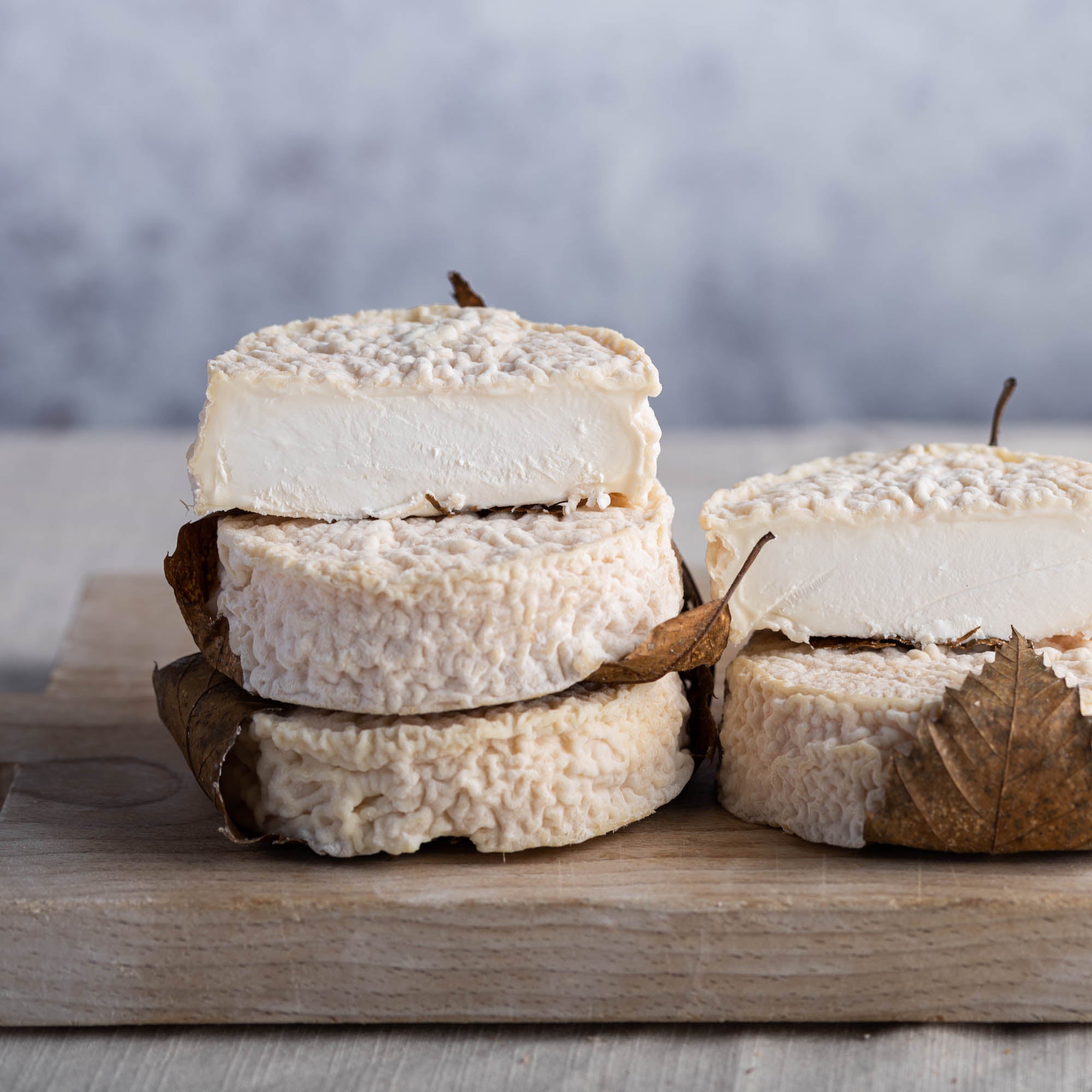 Cut and whole pieces of Mothais sur Feuille goat's cheese on a wooden board.