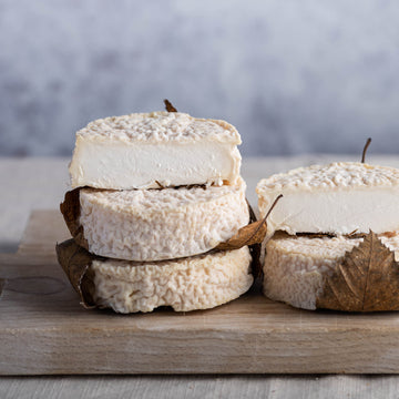 Cut and whole pieces of Mothais sur Feuille goat's cheese on a wooden board.