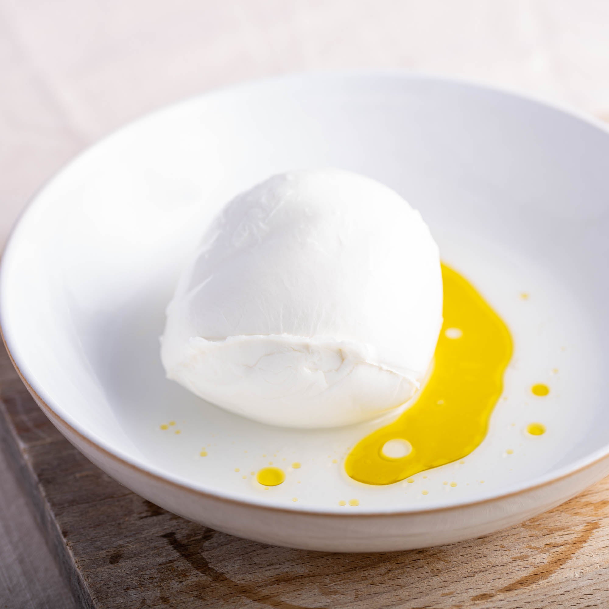 A whole Mozzarella cheese on a plate drizzled with some olive oil.