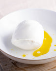A whole Mozzarella cheese on a plate drizzled with some olive oil.