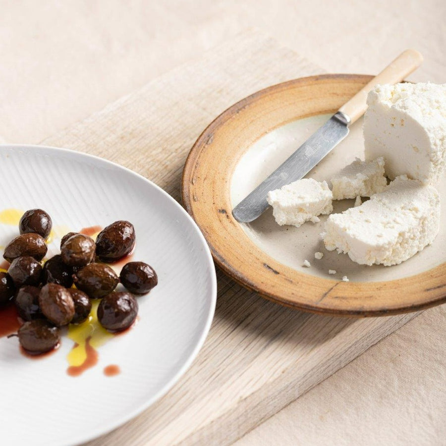 Plates of black nyons olives and feta cheese on a wooden board.