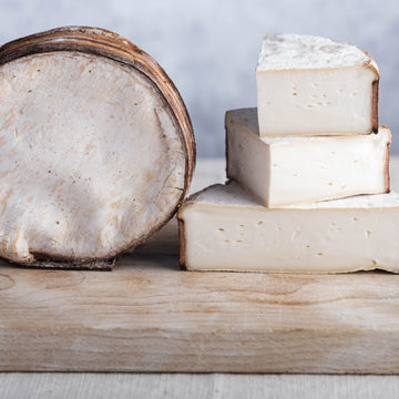 Cut pieces and a whole Placherin d'Areches goat's cheese on a wooden board.