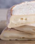 Pieces of soft reblochon cheese stacked up on a wooden board.