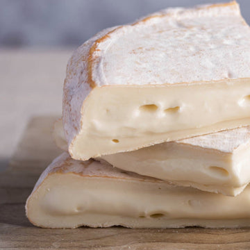 Pieces of soft reblochon cheese stacked up on a wooden board.