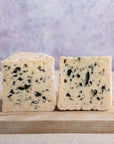 Two large pieces roquefort cheese on a wooden chopping board.