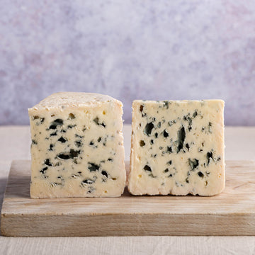 Two large pieces roquefort cheese on a wooden chopping board.