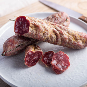 Cuts and larger pieces of Italian truffle salami on a white plate.