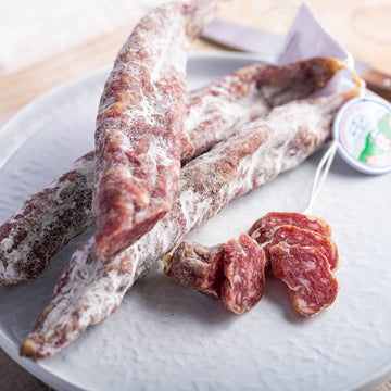 Slices and whole French saucisse seche salamis on a white plate.