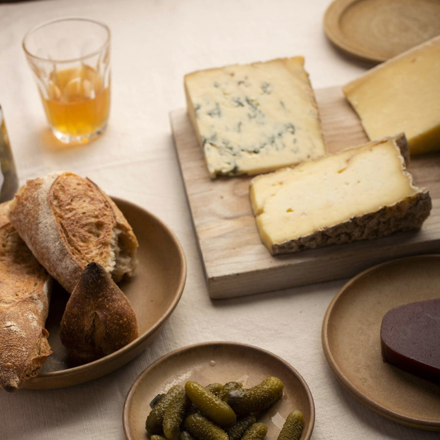 A selection of bread, cheese and cornichons on plates and a wooden board.