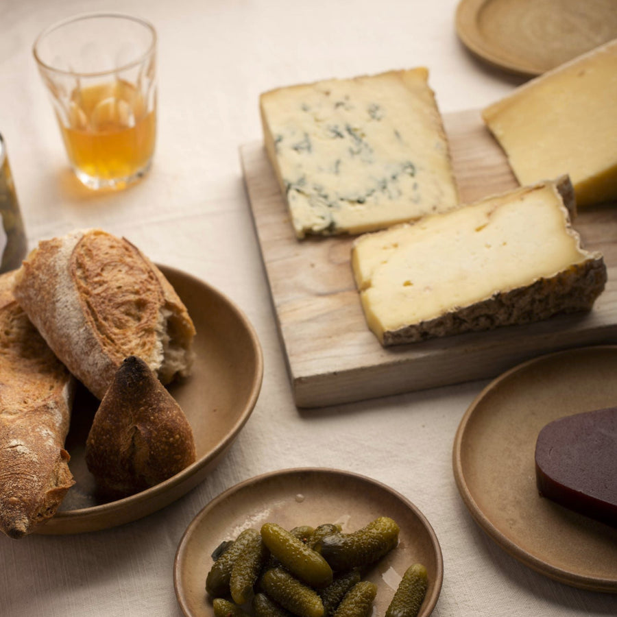 A selection of bread, cheese and cornichons on plates and a wooden board.