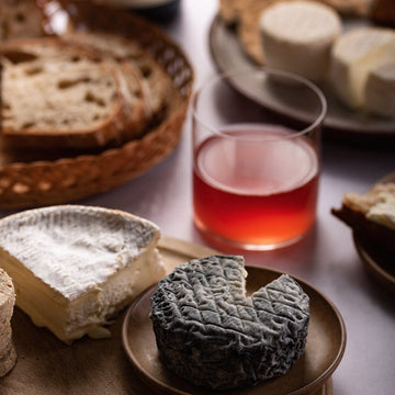 Cuts of cheese on a plate next to a glass of red wine.