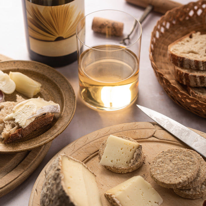 Cuts of Pecorino cheese and a knife on a wooden board, next to a glass of white wine.