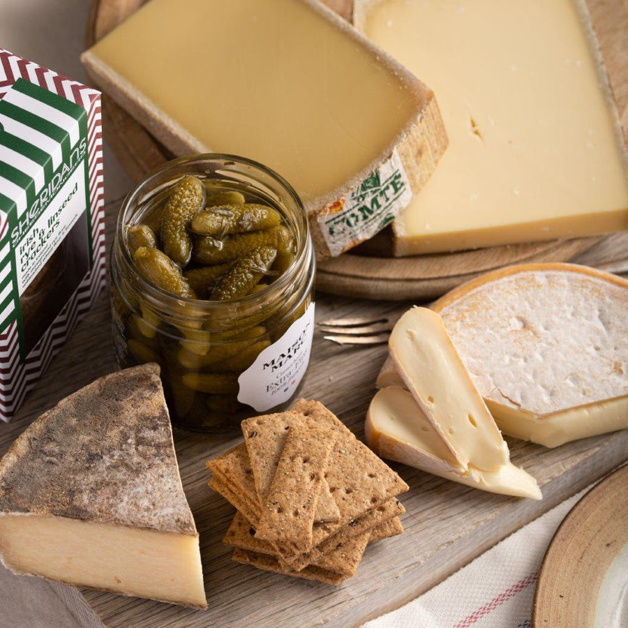 A selection of cheeses, cornichons and biscuits on a wooden board.
