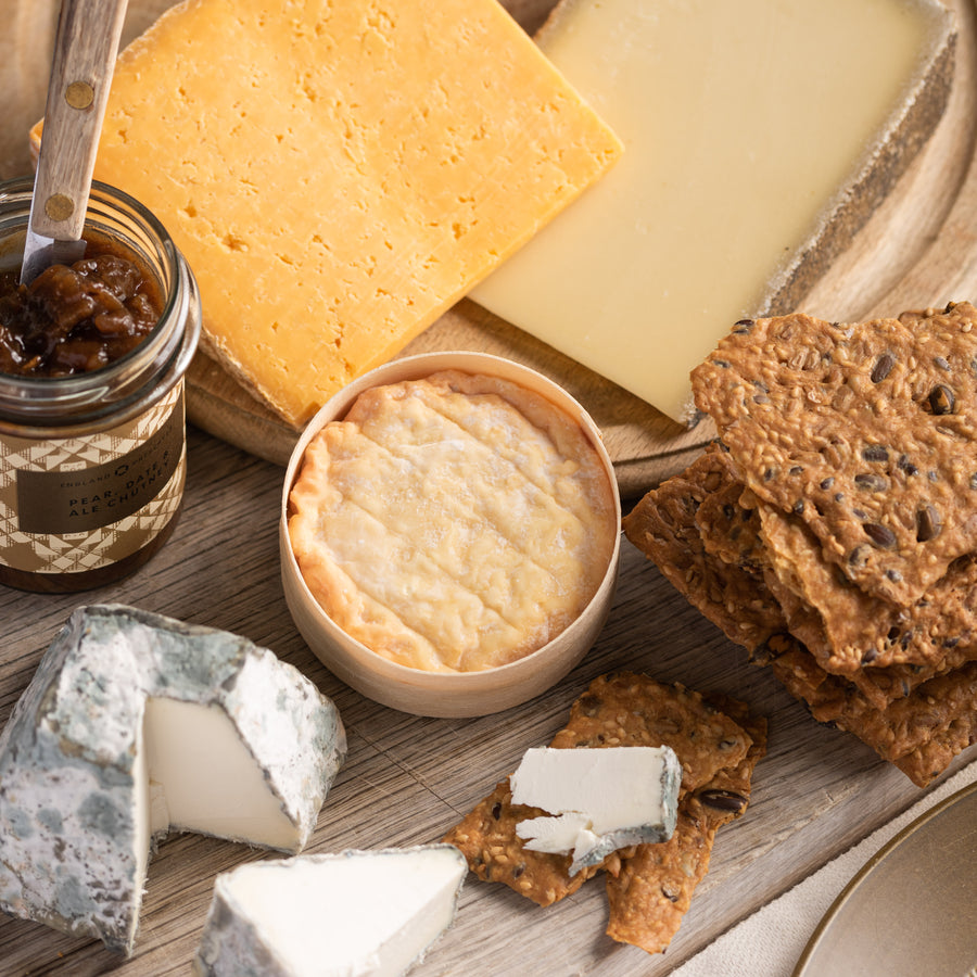 A selection of cheese, biscuits and chutney on a wooden board.