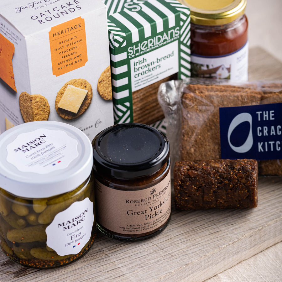 A selection of biscuits for cheese and jars of cornichons and pickle on a wooden board.