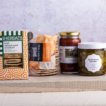 A selection of biscuits for cheese and jars of cornichons and chutney on a wooden board.