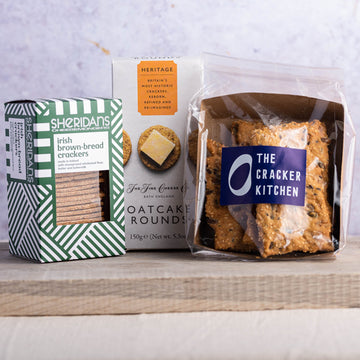 A selection of 3 different packets of biscuits for cheese on a wooden board.