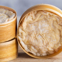 A close up of the orange wrinkly rind of St. Cera cheeses in their round wooden boxes, stacked up on a wooden board.