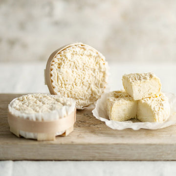 Whole and cut pieces of St. Jude soft cow's milk cheese on a wooden board.