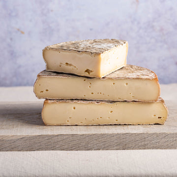 Large cuts of St. Nectaire cheese stacked up on a wooden board.