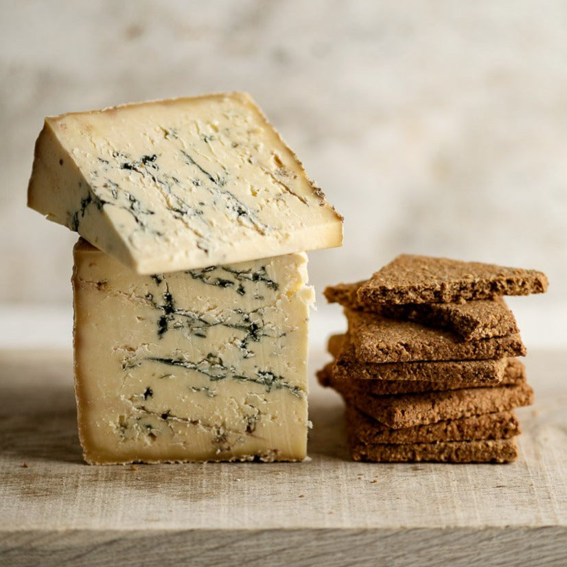 Pieces of Stichelton blue cheese and a pile of biscuits on a wooden board.