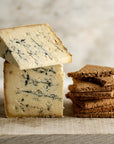 Pieces of Stichelton blue cheese and a pile of biscuits on a wooden board.