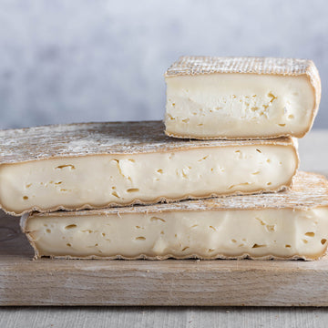 Cut pieces of Taleggio cheese on a wooden board.