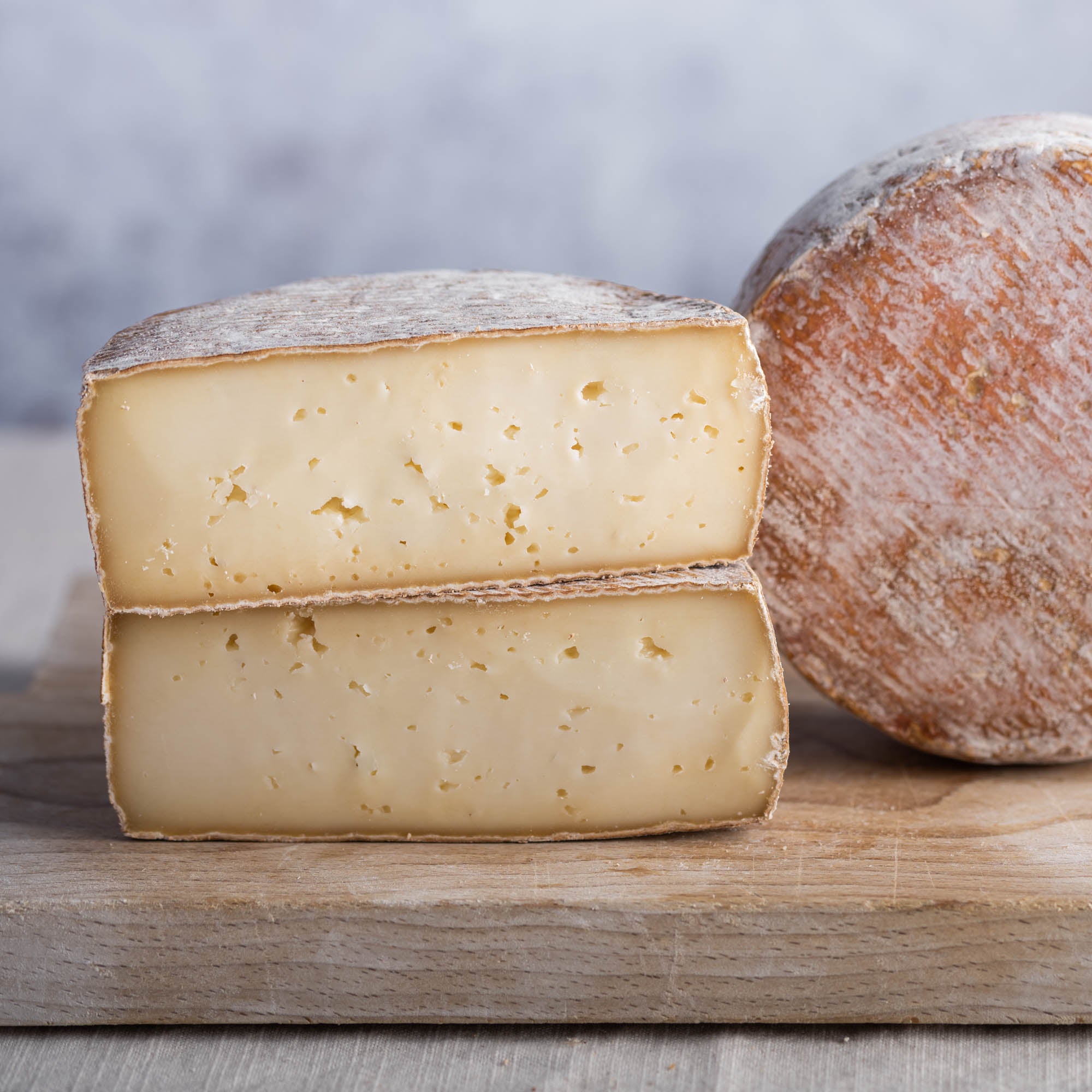 The cut faces of a Tommette Elutcha ewe's milk cheese on a wooden board.