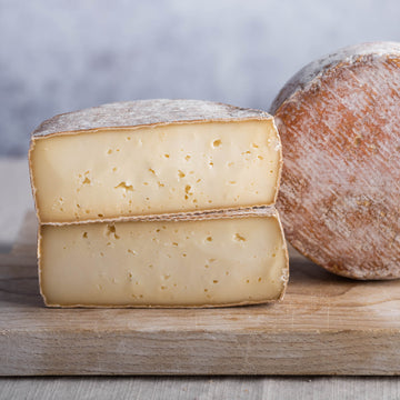 The cut faces of a Tommette Elutcha ewe's milk cheese on a wooden board.